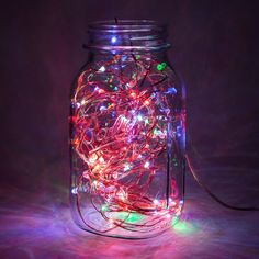 a glass jar filled with lots of lights on top of a table next to a cord