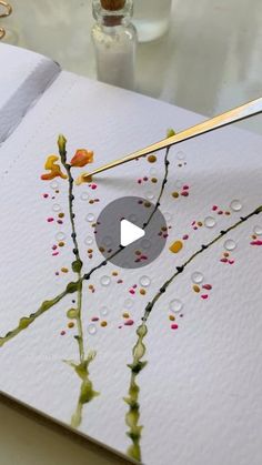 an open book with watercolors and gold scissors on it, next to some flowers