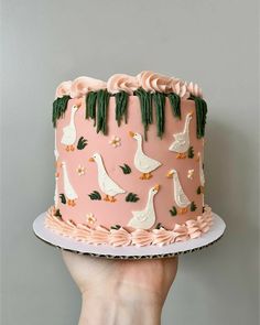 a hand holding a pink cake with white geese on it