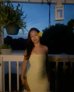 a woman in a yellow dress standing on a porch with a flower in her hair