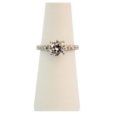 an engagement ring with three stones on top and two diamonds in the middle, sitting on a white pedestal