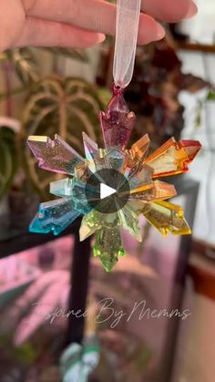 a hand holding a glass ornament with multicolored crystals on it's side