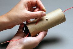 two hands are holding a roll of paper and some red thread on the end of it