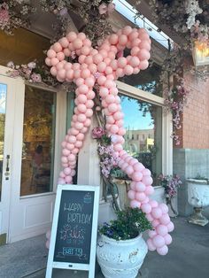 pink balloons are tied to the side of a building in front of a chalkboard sign