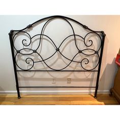 a black iron headboard with scroll designs on the top and bottom, against a white wall