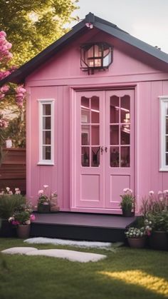 a pink shed with white trim and windows on the front door is surrounded by potted flowers