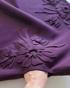 a purple dress with flowers on it is being held up by someone's hand