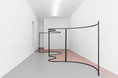 an art installation in a white room with pink flooring and black curved metal structure