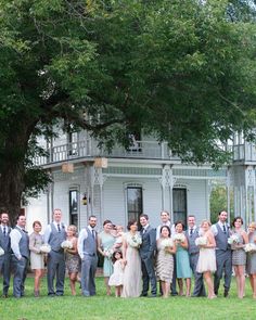 a large group of people standing in front of a white house with trees and grass