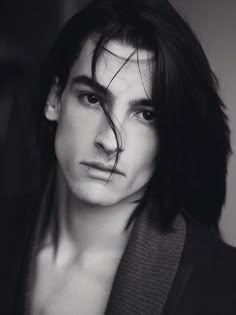 a black and white photo of a man with long hair wearing a sweater looking at the camera