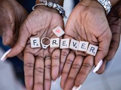 two hands holding scrabble letters spelling forever and wedding rings on top of them