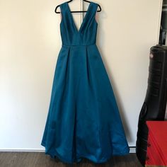 a teal dress hanging on a wall next to a red chair and black suitcase