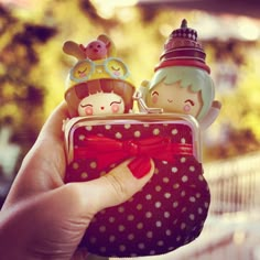 a hand holding a small purse with two dolls in it