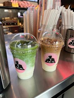 two iced drinks sitting on top of a metal counter next to cups with straws in them