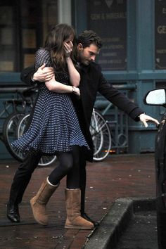 a man and woman walking down the street in front of a car with their arms around each other