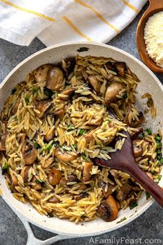 a pan filled with pasta and mushrooms on top of a table next to a wooden spoon