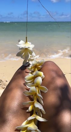 the back of a person's legs with white flowers on them and water in the background