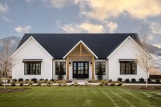 a white house with black shingles and windows on the front lawn, surrounded by mountains