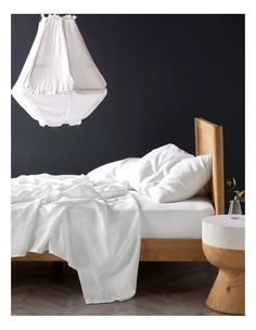 an unmade bed with white sheets and pillows in a dark room, hanging from the ceiling