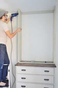 a man is using a power drill to paint a white closet with drawers and drawers