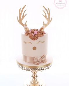 a white cake with pink flowers and antlers on top is sitting on a stand