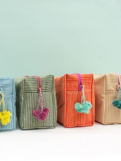 five small bags with tassels and pom - poms are lined up in a row