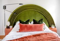 a green headboard with two orange pillows on top of it and a white bed in the background