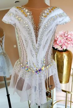 a white dress with gold and silver beads is on display next to a flower vase