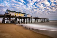 a long exposure photo of a pier with birds flying over it and the ocean in the foreground