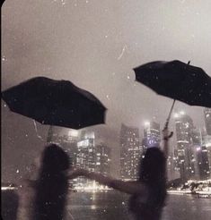 two people holding umbrellas in front of a cityscape at night with rain falling on them