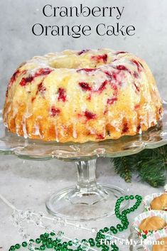 a cranberry orange cake sitting on top of a glass platter next to cookies