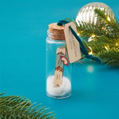 a small glass jar filled with snow next to a christmas ornament on a blue surface