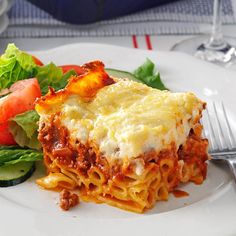 a white plate topped with lasagna covered in sauce and cheese next to a salad