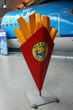 french fries sitting in a red container on top of a metal stand next to an airplane