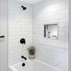 a bathroom with white tile and black faucet shower head in the bathtub