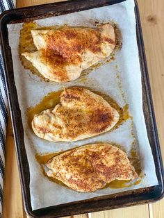 two pieces of chicken sitting on top of a baking pan covered in oil and seasoning