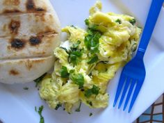 a plate with eggs, bread and a blue fork on the table next to it