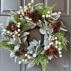 a wreath with pine cones, berries and greenery is hanging on the front door