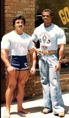 two men standing next to each other in front of a building