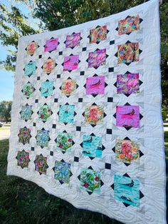 a quilt is hanging on the side of a tree in front of some grass and trees