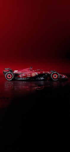 a red race car is shown on a black surface with a red light in the background