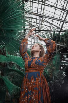 a woman in an orange and blue dress reaching up into the air with her hands