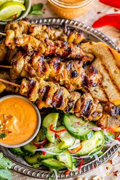 grilled chicken skewers on a platter with cucumbers and sauce