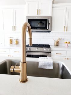 a kitchen with white cabinets and gold faucet, stainless steel sink and microwave