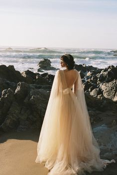 a woman standing on top of a beach next to the ocean wearing a wedding dress