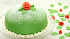 a green cake on a glass plate with red flowers and leaves around it, surrounded by icing