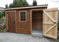 a wooden shed with an open door and brick walkway leading to the front yard area