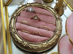 a pink ring box sitting on top of a table next to other rings and jewelry