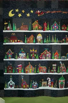 a quilted wall hanging with houses and christmas trees on it's sides in front of a window