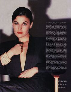 a woman in a black suit and gold bracelets posing for a magazine page with her hands on her chest